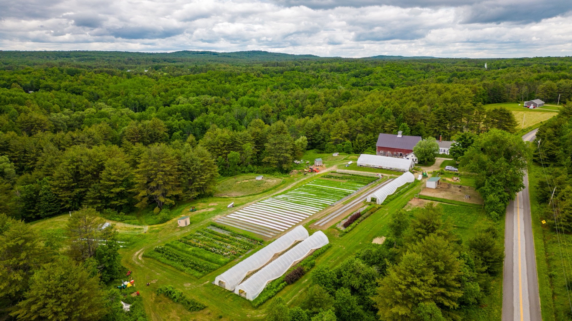 The farm from above — greenhouses, rows and the barn among the trees
